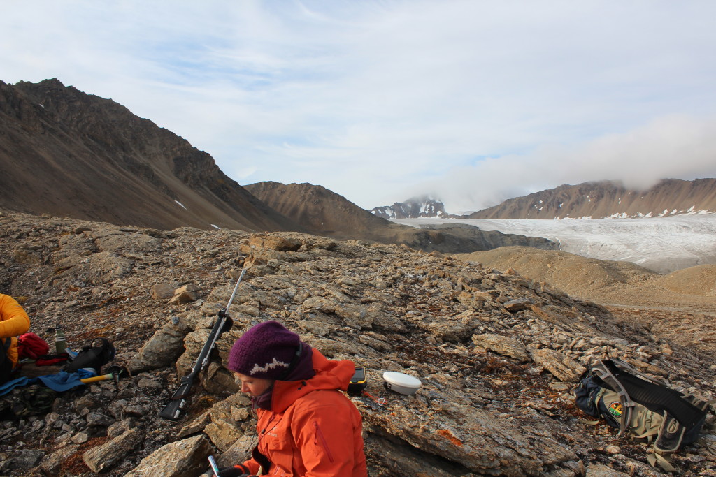 A picture taken looking outside at a moraine composed of billion-year-old glacial tillite and banded iron formations in the middle ground, and Socttbreen Glacier in the background.