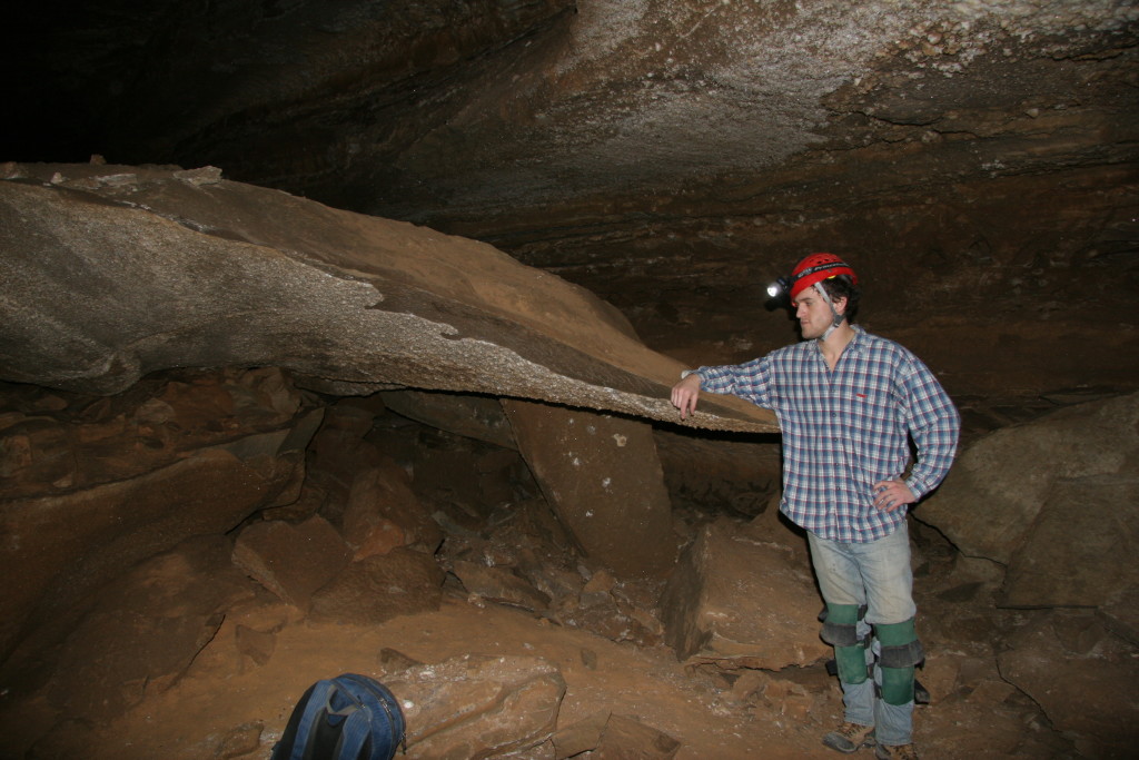 The author resting an arm on a large piece of the ceiling that had fallen.  A ~1-2cm gypsum crust is located on the underside of the slab.  In some areas of the cave, gypsum forms in cracks in the ceiling.  As it grows, it wedges the rock apart, driving collapse of the ceiling.