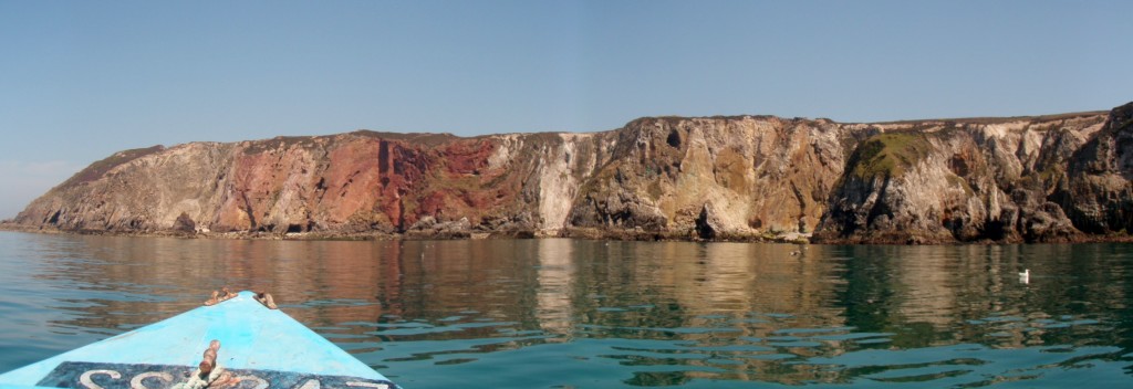 View of Cligga Head from a boat. The granite outcrops to the north (left), with the sheeted Sn-W and polymetallic sulphide veins towards the centre (red) and the country rock and elvans to the south (right).