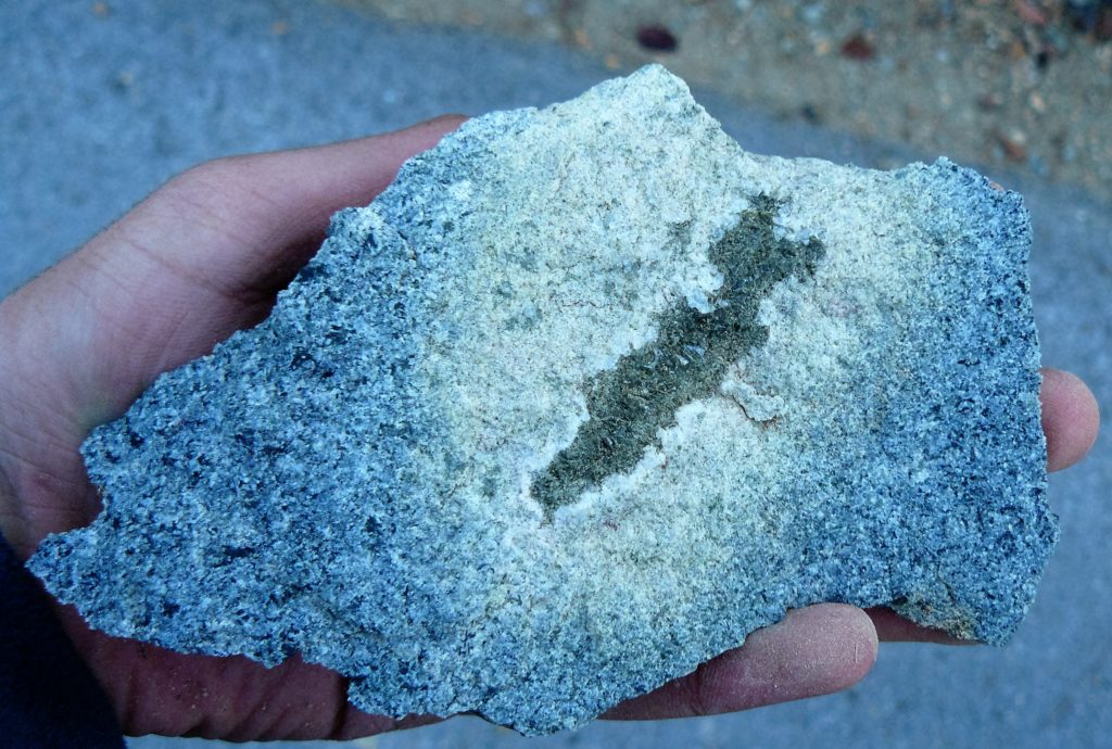 A grey plagiogranite altered to white-green epidosite. The internal cavity is filled by green epidote and allanite, rimmed by a thin selvage of white quartz.