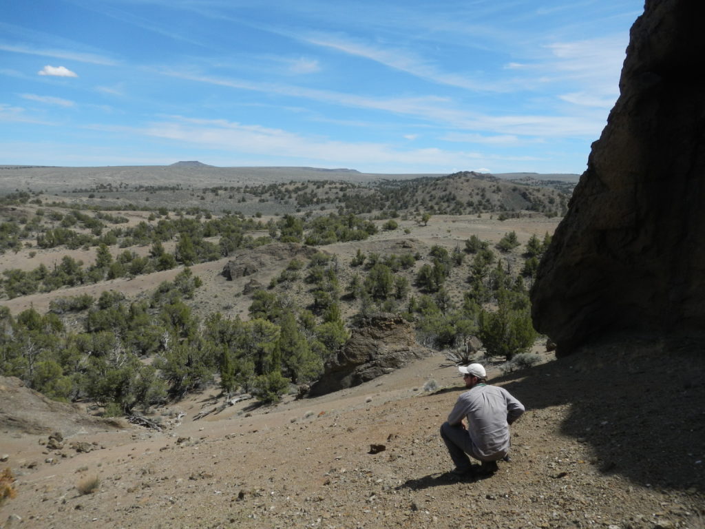 Matthew Nikitczuk pondering Oregonian geology from within the Black Hills. A volcano with a flat lava cap top is visible in the distance. Photo by Nevena Novakovic.