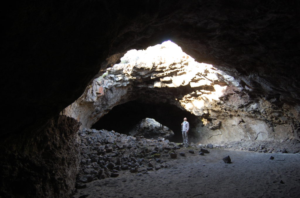 Matthew Nikitczuk standing inside the Derrick Caves lava tube. A large sky light can be seen in the roof of the lava tube letting the sunlight in. Photo by Nevena Novakovic.