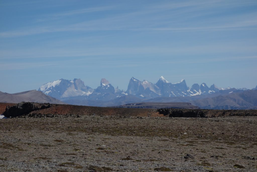 The peaks of Torres del Paine (background) seen from atop a basalt plateau (foreground). The Torres del Paine preserve an ancient magma chamber spectacularly exposed in 3-D. Even 150 km away, we could distinguish the intrusive magmatic rocks (pale colours) and the sedimentary rocks they were intruded into (dark colours). 